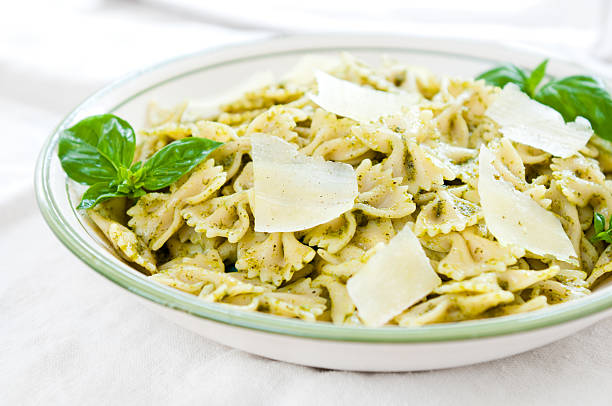 A bowl full of farfalle bowtie pasta tossed in a pesto sauce.  Garnished with shaved cheese and a sprig of fresh basil.