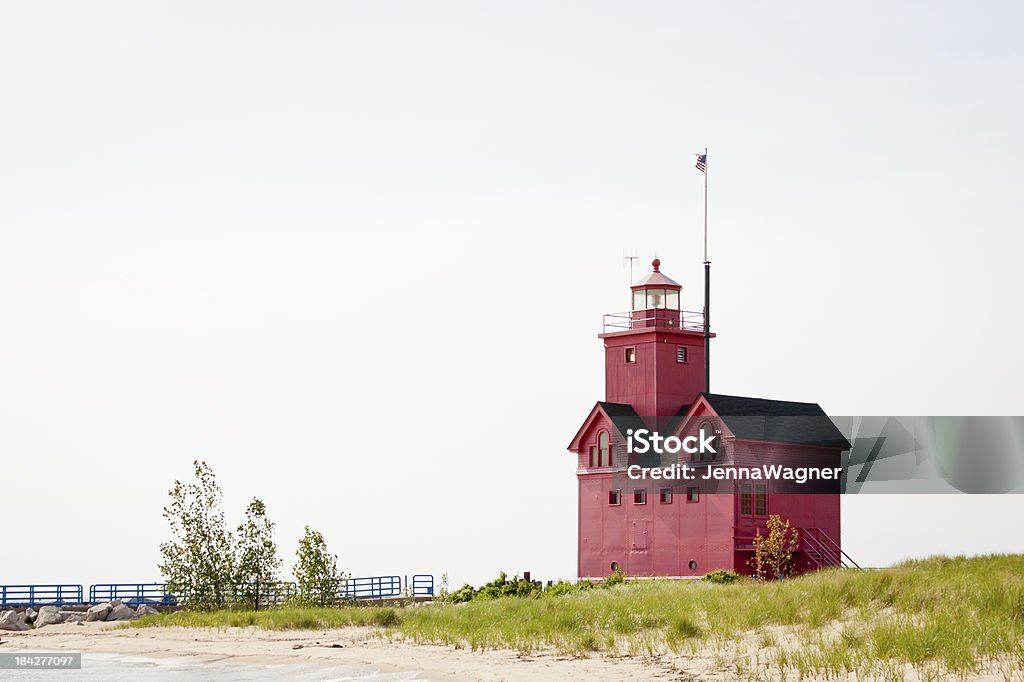 Big Red Lighthouse on Beach Red lighthouse on the Lake Michigan coast in western Michigan. The sun is loww on the horizon casting soft light and highlighting the deep colors of the coast and lighthouse. Big Red Lighthouse Stock Photo