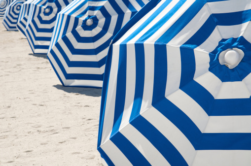 Bright blue and white striped beach umbrellas stand in a graphic row on the sand