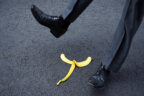 Businessman Slips on Banana Peel Businessman makes a dramatic slip on yellow banana peel on black asphalt slapstick comedy stock pictures, royalty-free photos & images