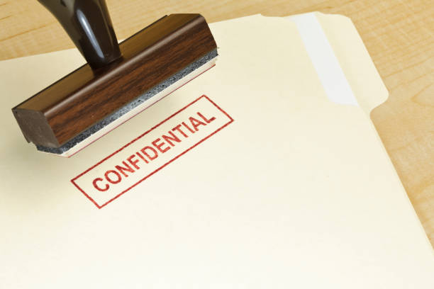 A manilla folder with the word CONFIDENTIAL stamped on it in red ink, with the rubber stamp that stamped it, above.