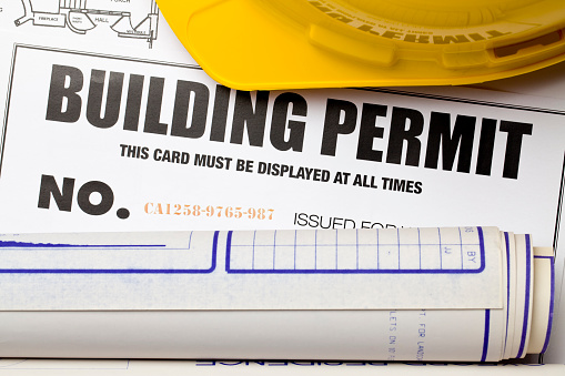 Building permit with hardhat and blueprints. Certificate was created by photographer with a graphics program. Code number is fictitious.