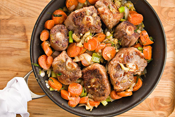 Browning Oxtails And Vegetables For Soup "An overhead close up of a large frying pan containing a colorful mixture of browned oxtails and vegetables, the makings for a flavorful  oxtail soup. Isolated on a wooden surface." wild cattle stock pictures, royalty-free photos & images