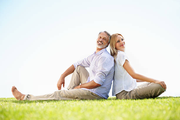 Full length of lovely mature couple sitting back to back in park