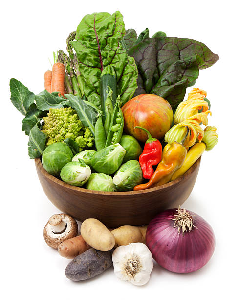 Variety of vegetables in a rustic wooden bowl including, chard, carrots, tomato, swash, zucchini, green peas, peppers, potatoes, onion, garlic, mushrooms, brussel sprouts and romanesco.