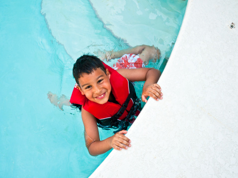 Cute boy looking at camera from the pool while wearing his life vest.