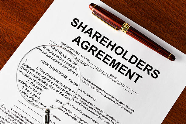 Magnifying glass on shareholders agreement Shareholders agreement on table shareholder photos stock pictures, royalty-free photos & images