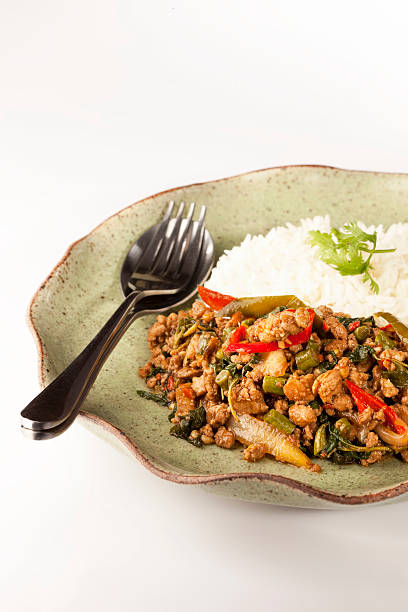 Pad Krapao Moo, spicy stir-fried pork with Thai/Holy basil and steamed white rice. In Thailand people use a fork and a spoon, rather than a knife and a fork, to eat their meals. This meal is served with a Thai traditional fork and a spoon. Shallow depth of field.