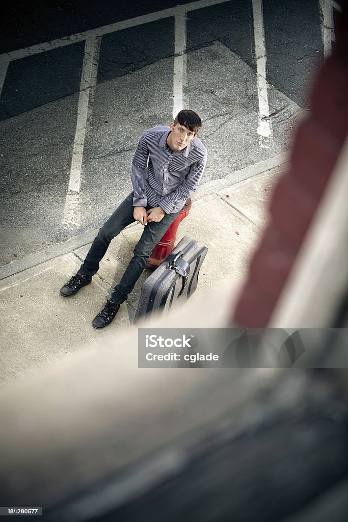 Waiting Young man sitting outside apartment window with suitcase City Stock Photo
