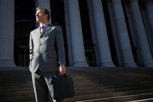 Lawyer businessman stands on set of dark steps with grand courthouse columns in the background