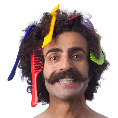 Portrait of man with long hair and handle bar mustache having many colored combs on head.He is smiling and his eyes are wide open.The photo was shot by a full frame DSLR camera in horizontal composition and edited to square on white background.