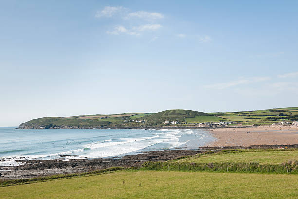 Croyde Bay Devon in Summer "View over Croyde Bay to the headland named Baggy Point behind. Shot on a afternoon Sunday in Summer, there are many people enjoying the beach and in the water. Croyde is on the North Devon coast and is a popular summer holiday and surfing destination." croyde photos stock pictures, royalty-free photos & images