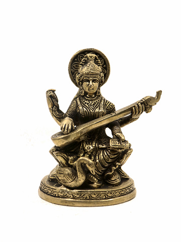 brass statue of saraswathi, goddess of knowledge, art, music, nature and wisdom sitting on a lotus near a swan playing veena instrument