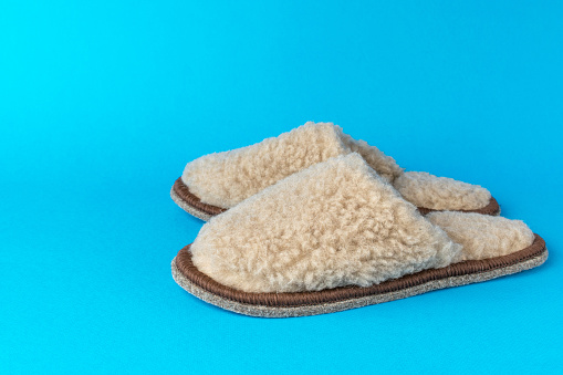 Beige slippers on a blue background. Comfortable shoes for home.