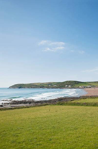 Croyde Bay Devon in Summer "View over Croyde Bay to the headland named Baggy Point behind. Shot on a afternoon Sunday in Summer, there are many people enjoying the beach and in the water. Croyde is on the North Devon coast and is a popular summer holiday and surfing destination." croyde photos stock pictures, royalty-free photos & images