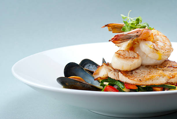 Broiled Seafood Seafood medley of shrimp, scallops, mussels and fresh fish over a bed of vegetables. crustacean stock pictures, royalty-free photos & images