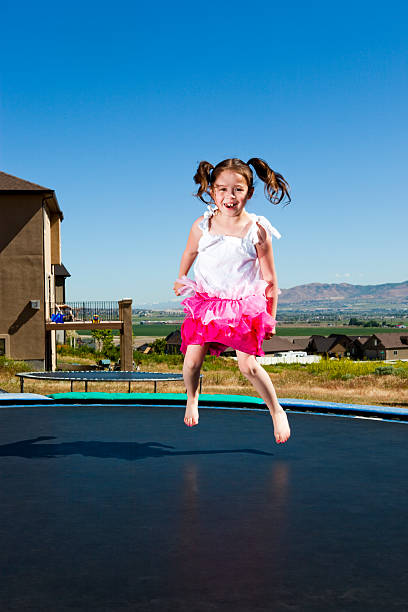 Serious young girl sitting on a trampoline after an injury, holding her leg with concern, in soft evening light, outdoors.