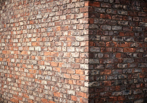 An old and weathered brick wall, with a right angle corner.