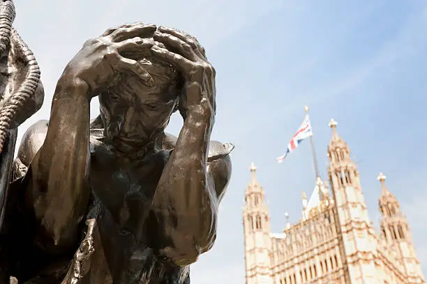 "low angle view on a detail of the famous sculpture The Burghers of Calais, Les Bourgeois de Calais by Auguste Rodin, Victoria Tower Gardens, Victoria tower on the background, London UK, XXXL image"