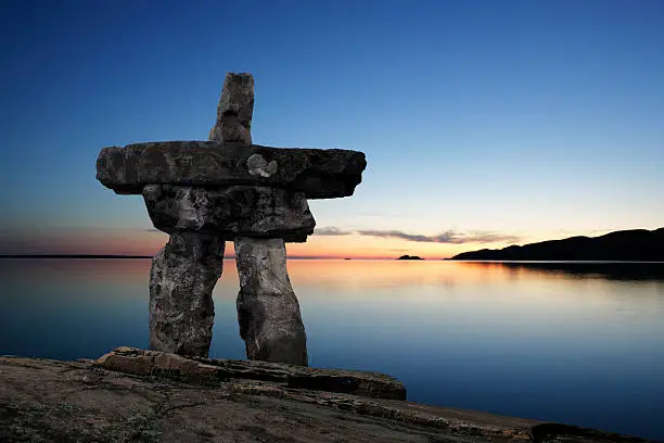 inukshuk in silhouette on hilltop overlooking lake at twilight (XL)