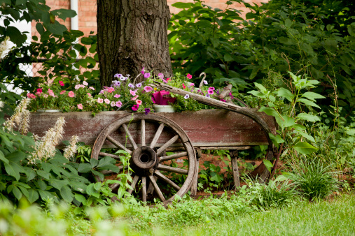 Beautiful flower garden with a rustic wooden wagon and wheel.