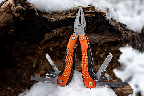 Multifunction pliers with other tools and knife on a old hollow tree covered with snow. Selective focus.