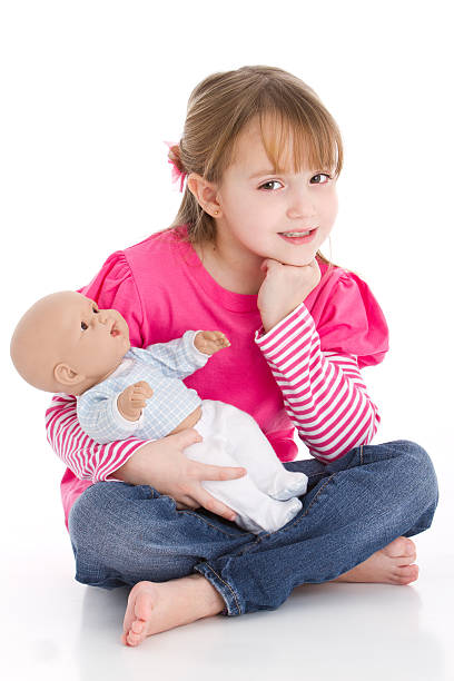 Young girl in pink sitting on floor and holding a baby doll Sweet little girl as a mom playing with a baby doll girl playing with doll stock pictures, royalty-free photos & images