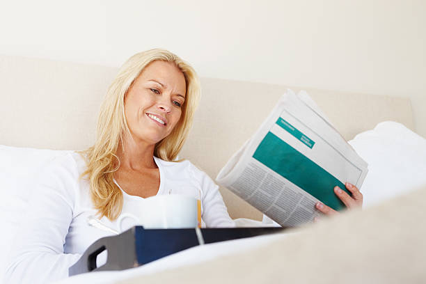 istock Mature woman in bed reading newspaper 184289349