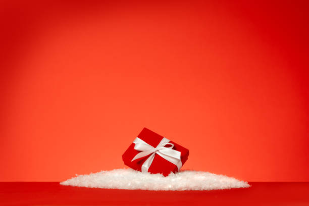 festive red gift box with white bow lying in the snow against red background. christmas or holiday celebration concepts. - fake snow imagens e fotografias de stock