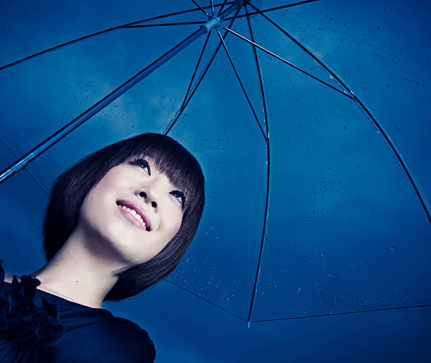 Portrait of a beautiful young Japanese woman holding an umbrella, staying out of the rain.