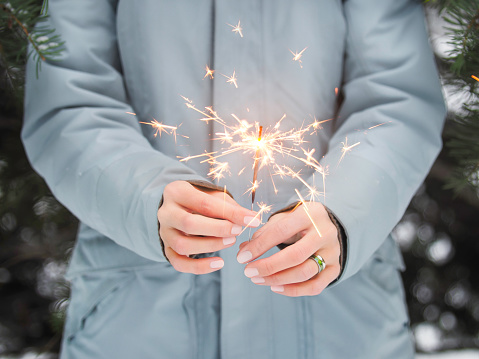Woman celebrates Christmas or New Year with bright sparkler. Bengal fire, traditional firework for winter holiday celebration outdoors.Smiling woman celebrates Christmas or New Year with bright sparkler. Bengal fire, traditional firework for winter holiday celebration outdoors.