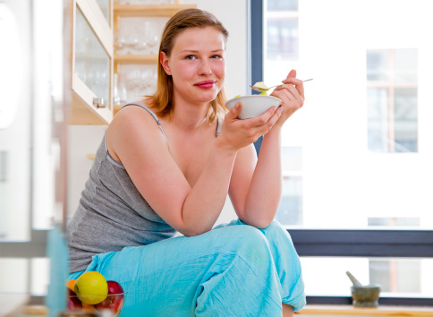 Slightly overweight woman eating a heathly breakfast while sitting in a modern kitchen.