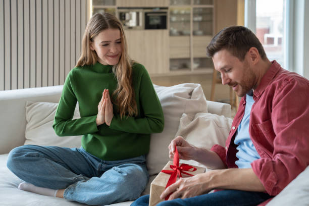 istock Surprised man unpack gift present, woman wait sitting on couch near with pray hands looking reaction 1842918803