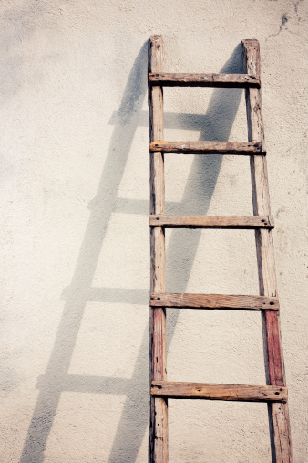 Old wooden ladders and shadow on textured concrete wall. Vintage look.