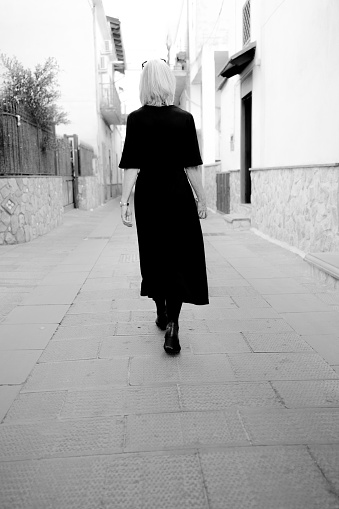Monochrome image of a mature woman in a black dress walking along the alleys of the town of Scafati, south of Naples, Italy.