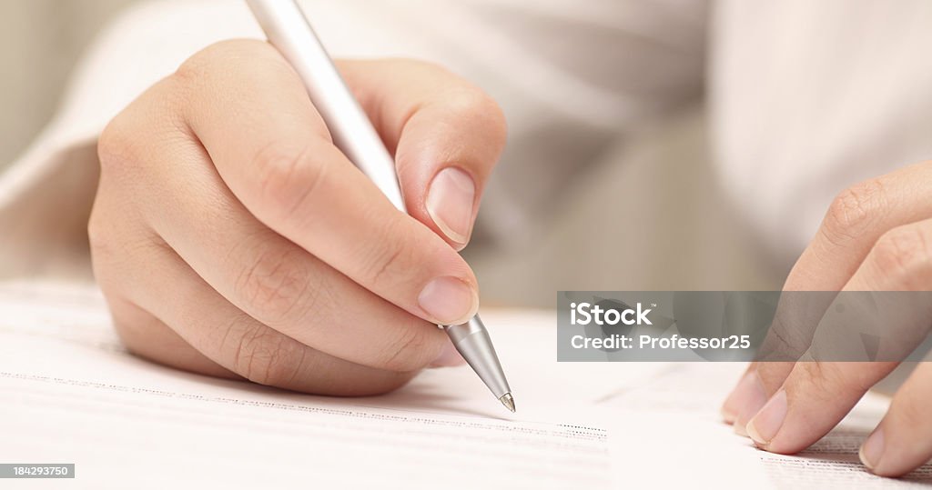 Woman about to sign a document with a silver pen. Businesswoman viewing the contract before signing. Close-up. Focus on pen. Shallow depth of field. Adult Stock Photo