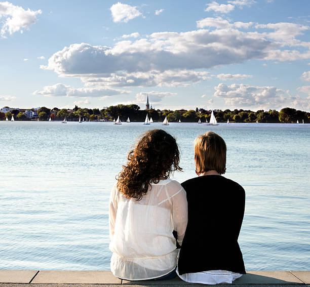 Girlfriends sitting on pier looking out over water Girlfriends sitting on pier looking out over water binnenalster lake stock pictures, royalty-free photos & images