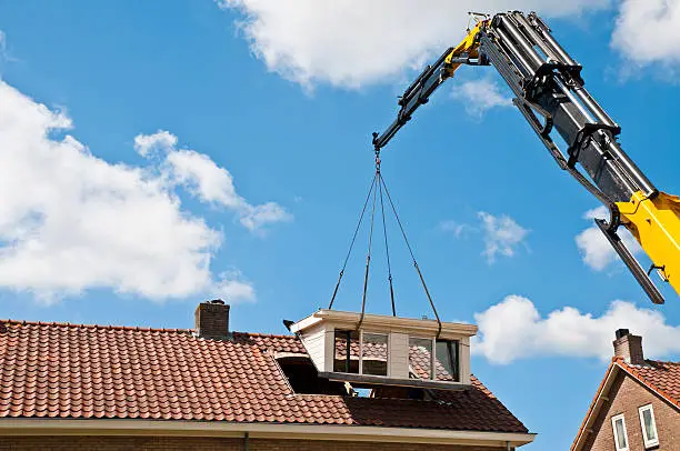 A prefab dormer is raised with a crane to a hole in a roof Similar images: