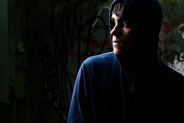 Moody serious teenage boy wearing a blue hoodie staring sullenly at the camera with earphones slung around his neck in a frontal portrait