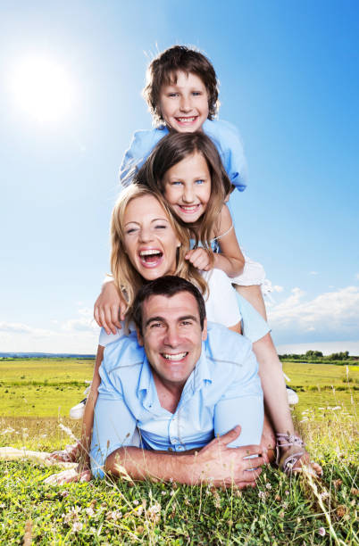 Portrait of happy family laying down one the other. People laughing and playing on meadow in a beautiful sun day.