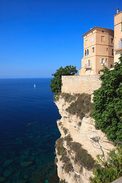 Houses on steep cliff with overhang in Bonifacio, Island of Corsica, France. Mediterranean sea. The old city of Bonifacio was built on steep cliffs looking directly to the neighbouring island Sardinia which is only 12 km (around 8 miles) away.