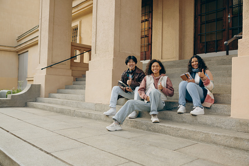 Happy students sitting on stairs outside library during study session and looks camera