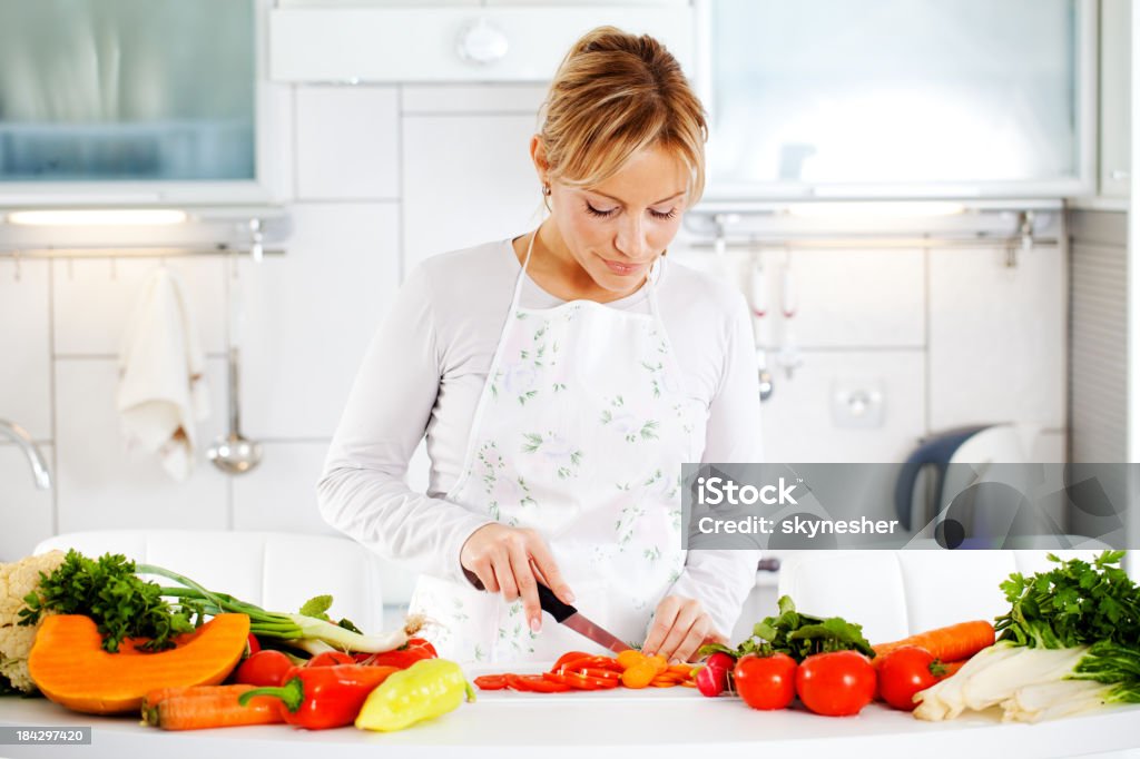 Young woman cutting carrots. Beautiful blonde is  preparing the salad in the kitchen. Adult Stock Photo