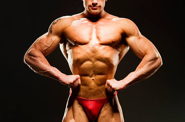 Body Builder Posing - Front Lat Spread Body building - a shirtless healthy man flexing his lateral back muscle. Black background. lat spread bodybuilder stock pictures, royalty-free photos & images