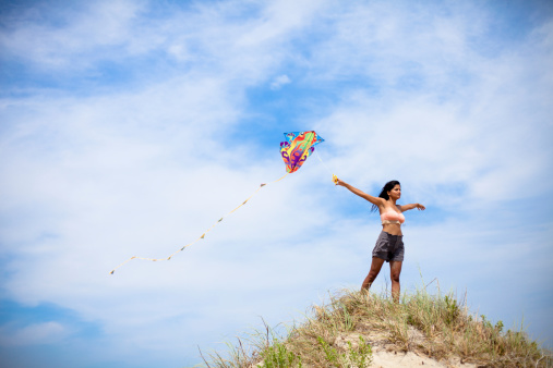 A beautiful Indian woman flying a kite on a summery blue sky day at the beach.See More: