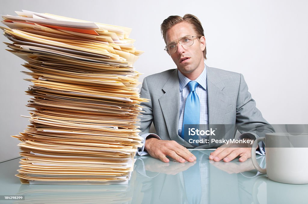 Empresário cansado Trabalhador de escritório, sentado na mesa olhando papéis - Foto de stock de Escrivaninha royalty-free