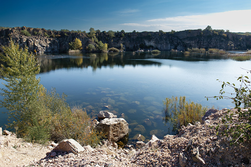 Landscape with a mountain lake. Clean transparent water of the river, rocky shore, blue sky. Rocks and trees are reflected in the lake. Travel, tourism, outdoor recreation.