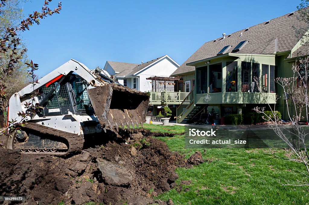 Bulldozer Scoops Dirt for a New Swimming Pool A small digger drops dirt removed from an excavation in back of a suburban house.  Digging Stock Photo