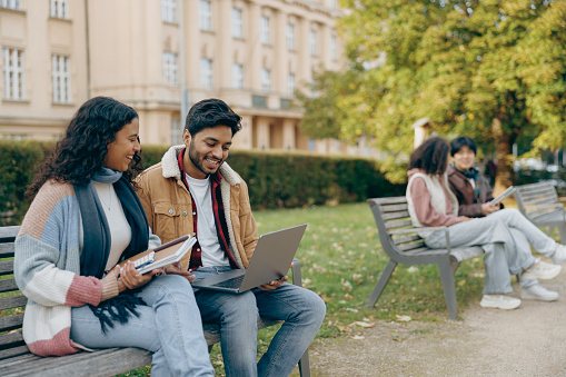 Smiling students with laptop is studying outdoors sitting near university. Education concept