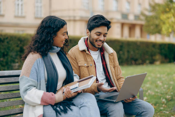 istock Smiling students with laptop is studying outdoors sitting near university. Education concept 1842999051